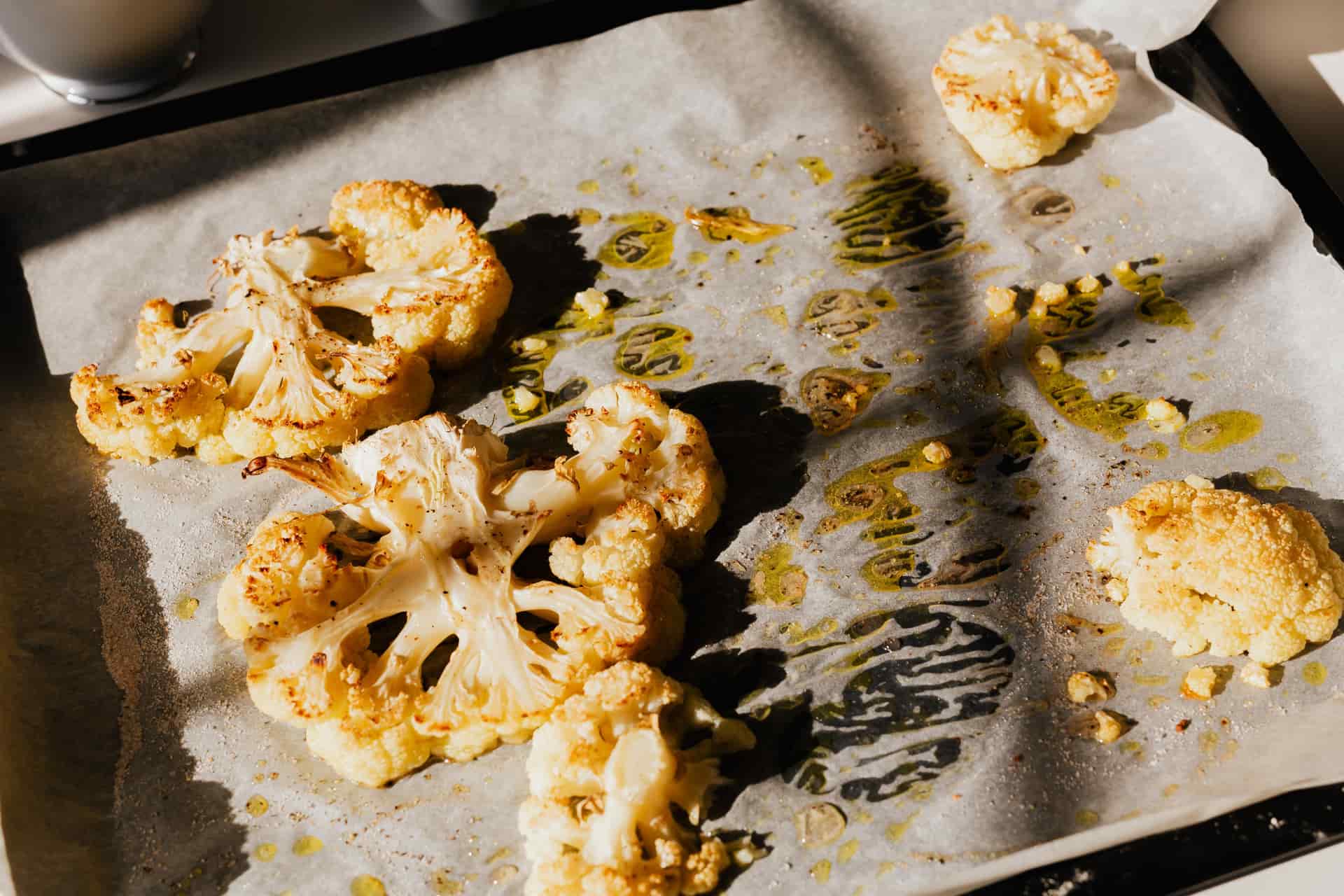 Golden roasted cauliflower slices on baking paper, seasoned with herbs