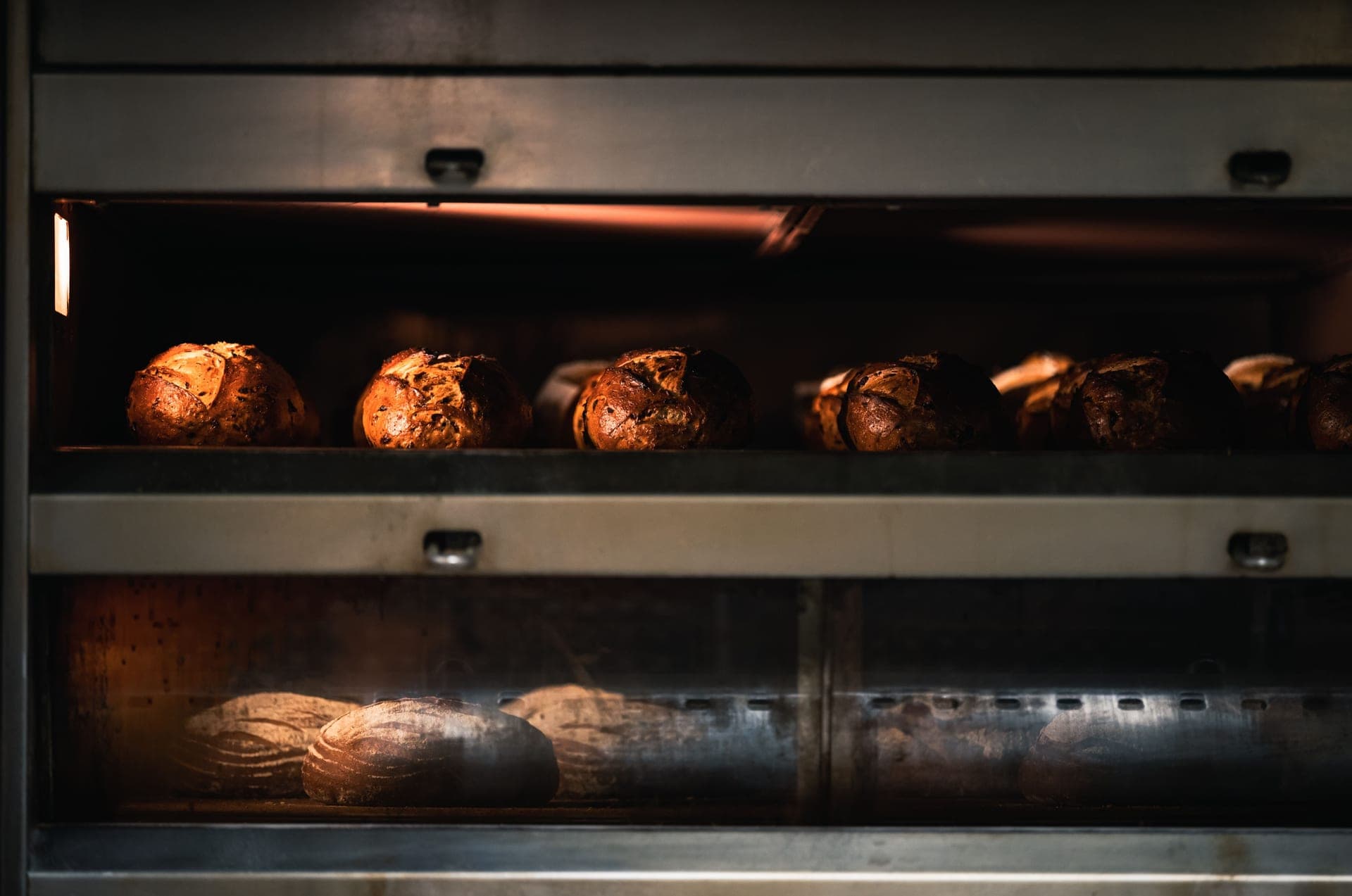 Loaves of bread baking inside a countertop oven, glowing warm through the door